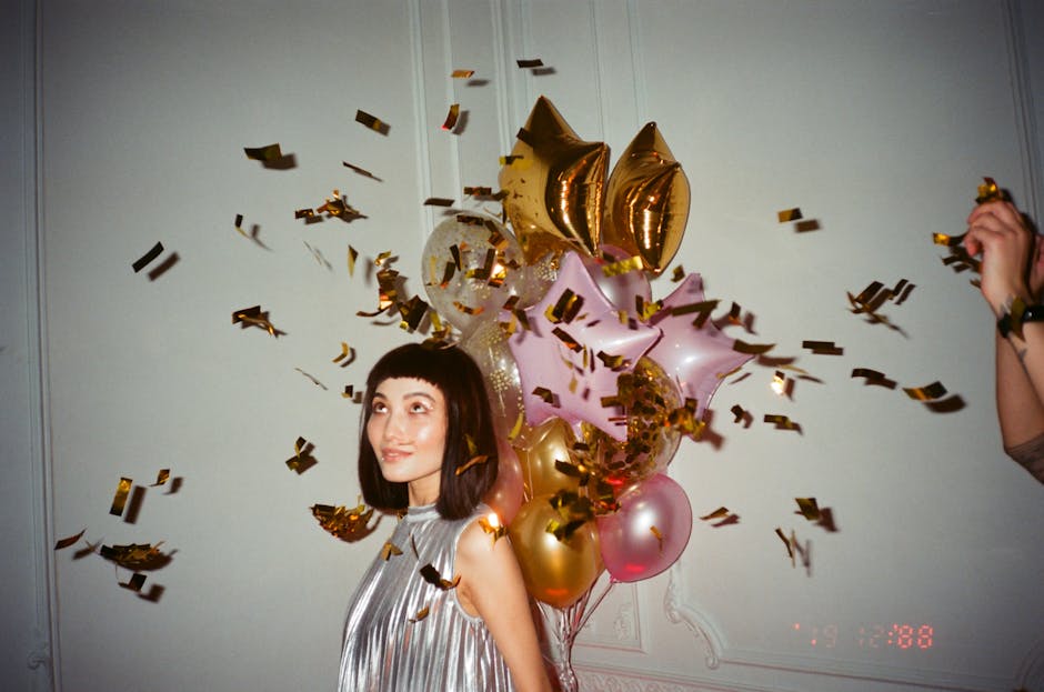 A young woman celebrating indoors with balloons and confetti, exuding joy and festive spirit.