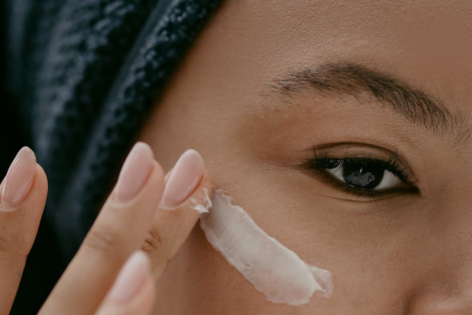 Extreme close-up of a woman applying cream to her cheek for healthy skin care.