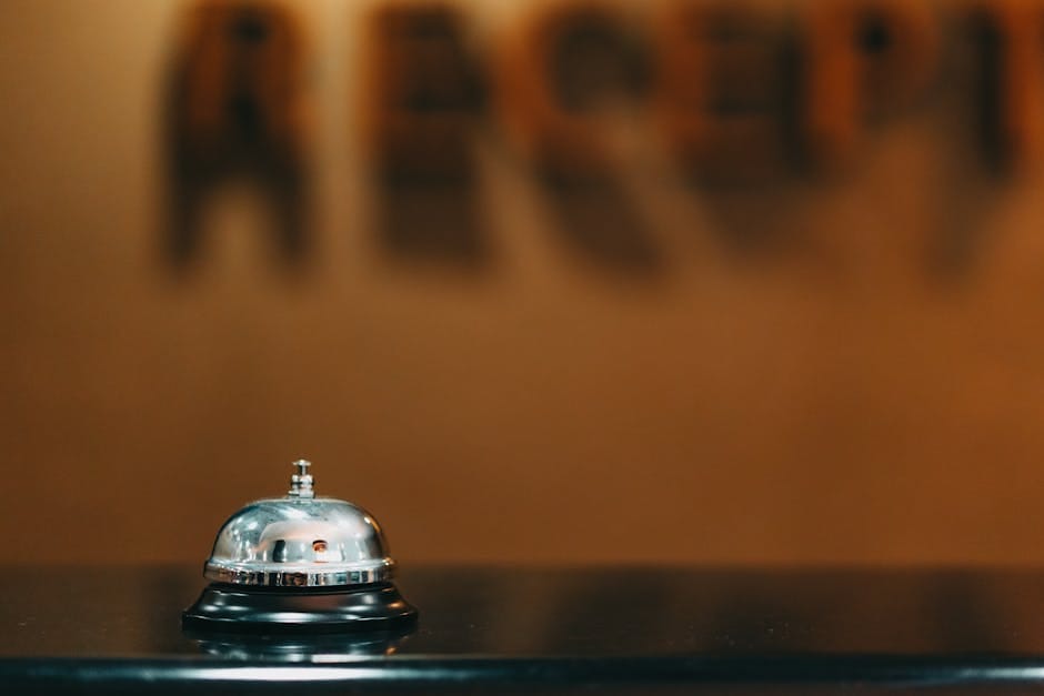 Close-up image of a silver hotel bell on a black surface with 'RECEPTION' blurred in the background.