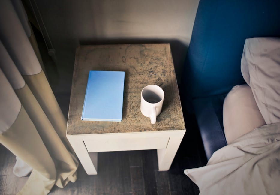 A serene bedroom setting featuring a book and mug on a rustic side table by the bed.